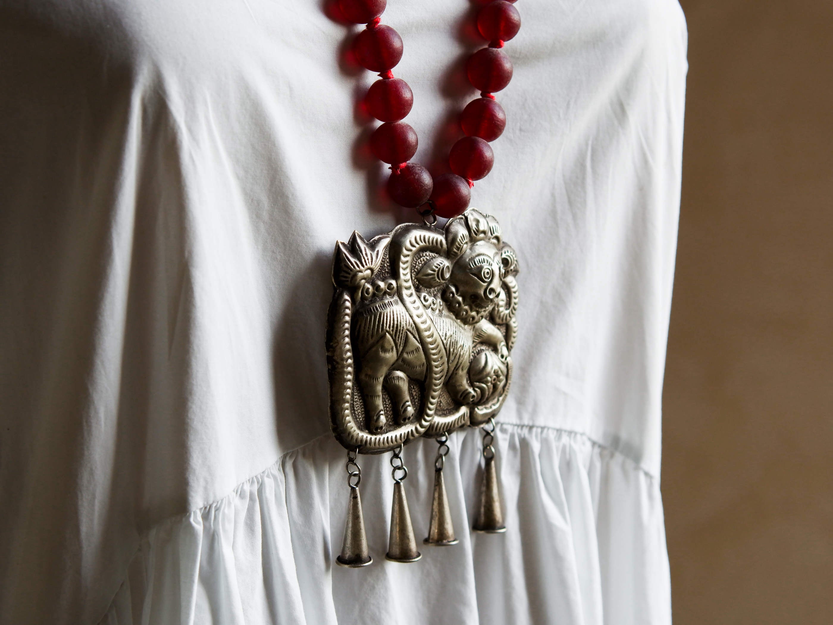collana indiana in tessuto, pasta vitrea e lega di argento fatta a mano, sfere in pasta vitrea e nodini in cotone pendaglio con figura mitologica della cultura tibetana buddista lavorato in lega di argento  lunghezza totale ( circonferenza ) 80 cm pendaglio 9 x 7 cm escluse campane campanelle 3 cm peso 230 gr