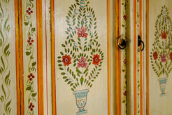 Dettaglio delle ante intagliate con motivi floreali a candelabra e finitura avorio su credenza coloniale in teak.