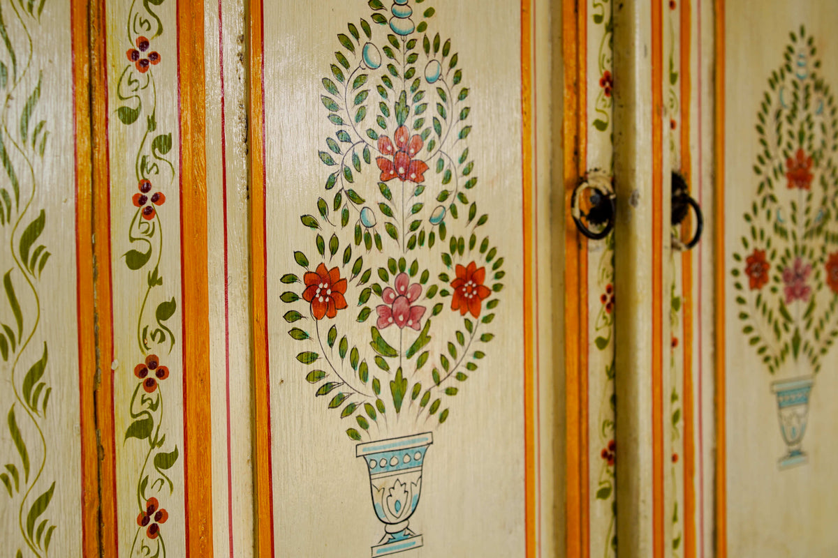 Dettaglio delle ante intagliate con motivi floreali a candelabra e finitura avorio su credenza coloniale in teak.