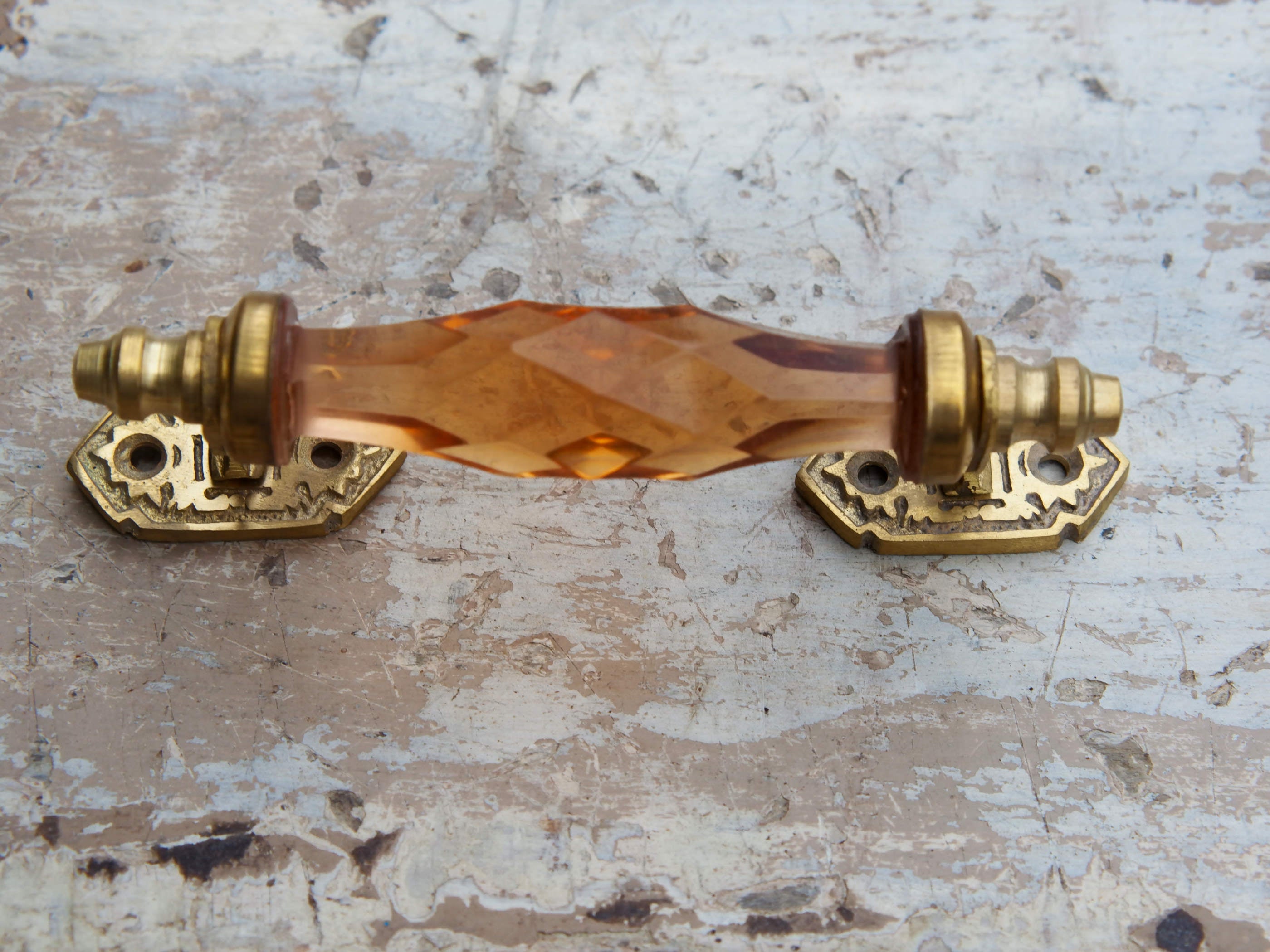 Maniglia in vetro lievemente sfaccettato di colore ambra su supporto in metallo color oro. Disponibile in altri colori come da foto.  dimensioni 14x5x3cm