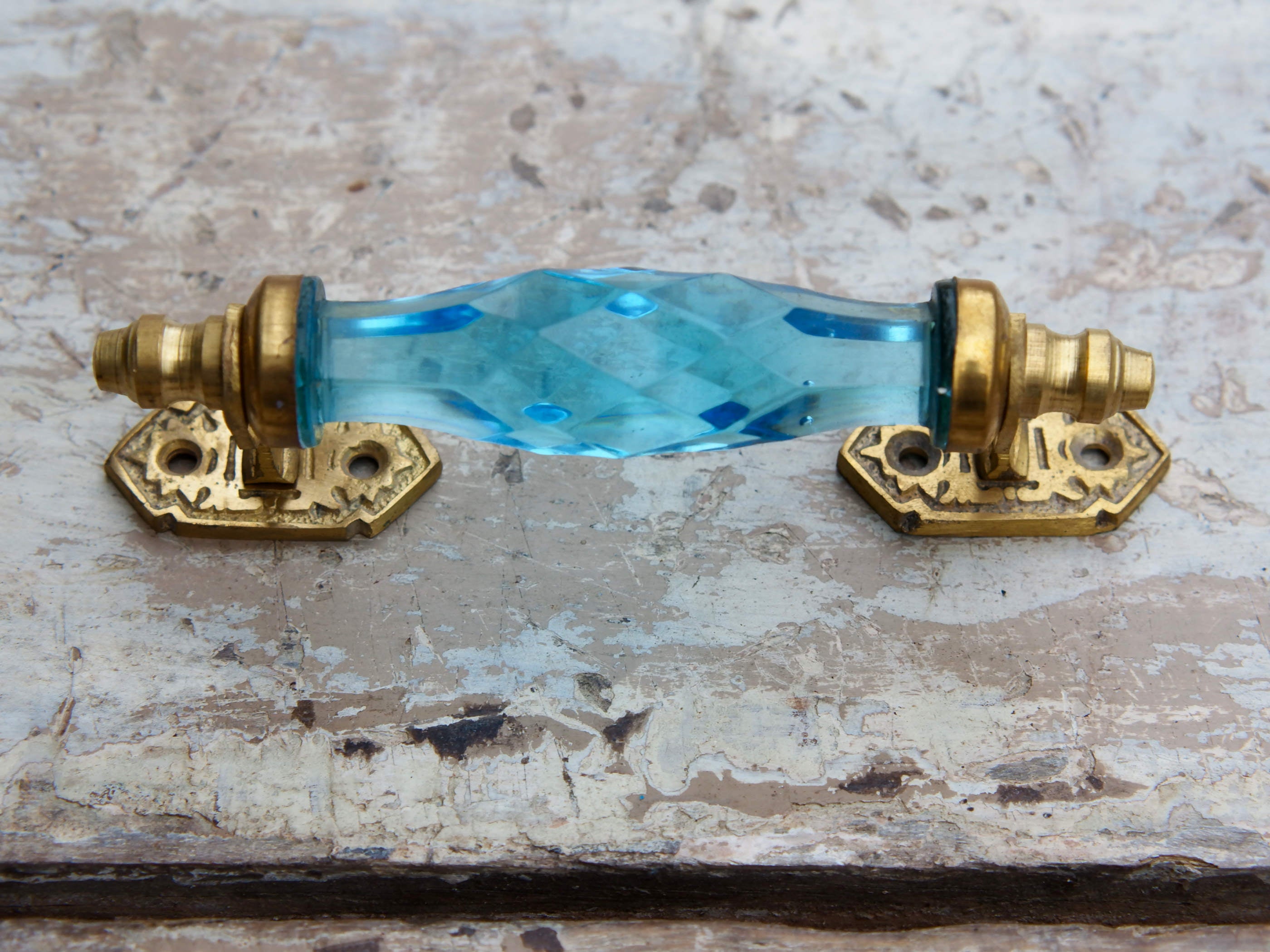 Maniglia in vetro lievemente sfaccettato di colore azzurro su supporto in metallo color oro. Disponibile in altri colori come da foto.  dimensioni 14x5x3cm