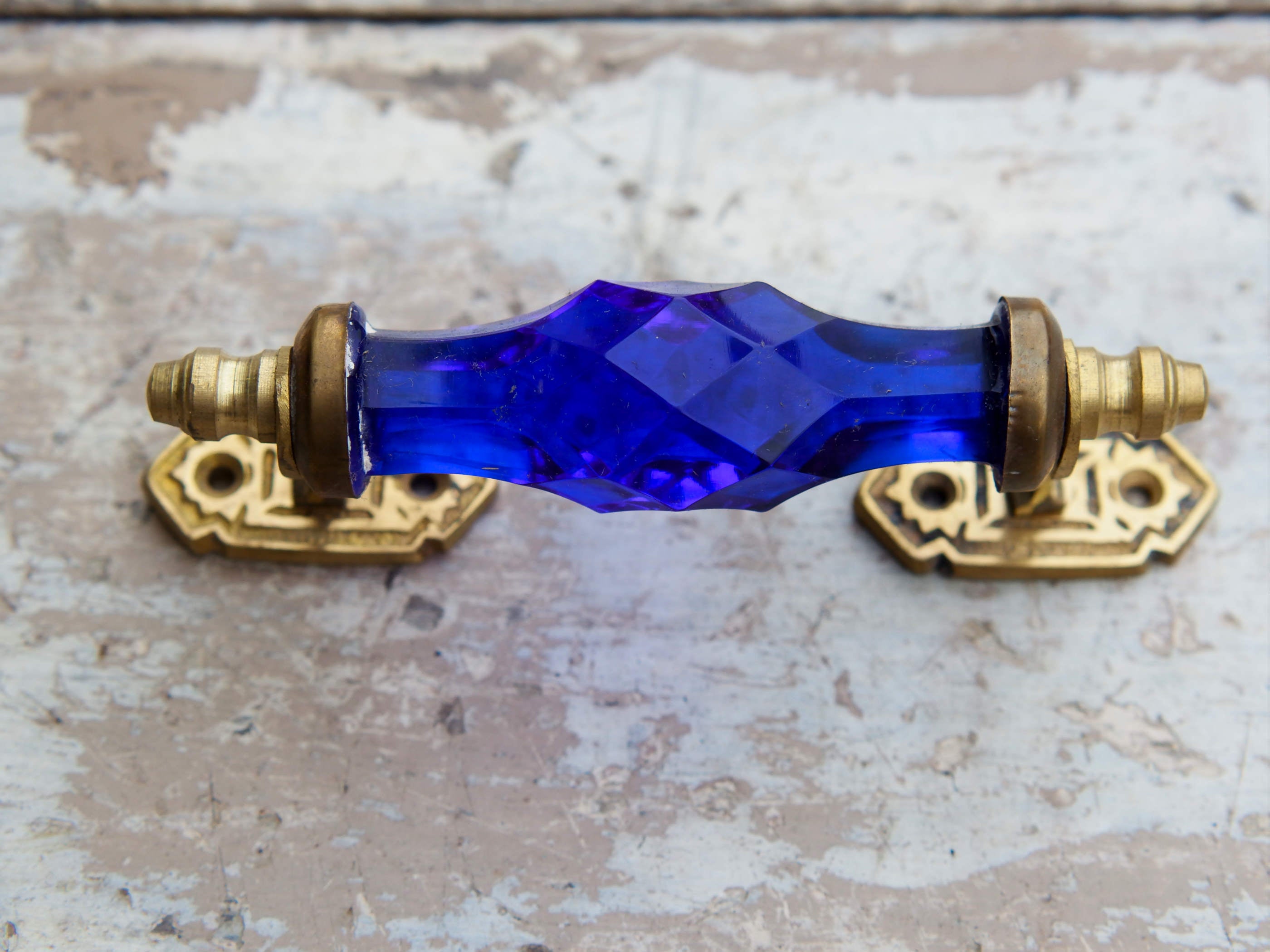 Maniglia in vetro lievemente sfaccettato di colore blu su supporto in metallo color oro. Disponibile in altri colori come da foto.  dimensioni 14x5x3cm