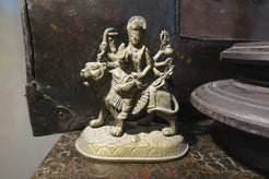 statuetta di Durga indiana in metallo inciso artigianalmente .   Presso la religione induista  "colei che difficilmente si può avvicinare" è una forma di Devi , ovvero della Madre Divina (che assume anche molte altre forme, tra cui Sarasvati , Parvati, Lakshmi, Kālī). È raffigurata come una donna che cavalca un leone, sebbene più raramente la si trovi raffigurata anche su una tigre, con numerose braccia mani che impugnano diversi tipi di armi e fanno dei mudrā (gesti simbolici fatti con la mano). Questa for