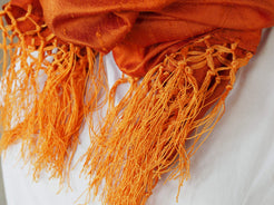 Scialle indiano in shantung di seta , un tessuto di seta selvaggia, di colore unito, caratterizzato da una superficie ruvida, molto irregolare e dall'aspetto grezzo di colore arancione.
