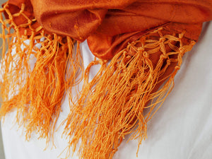Scialle indiano in shantung di seta , un tessuto di seta selvaggia, di colore unito, caratterizzato da una superficie ruvida, molto irregolare e dall'aspetto grezzo di colore arancione.