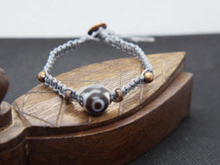 bracciale intrecciato con dzi in agata , chiusura a bottone regolabile in misura.