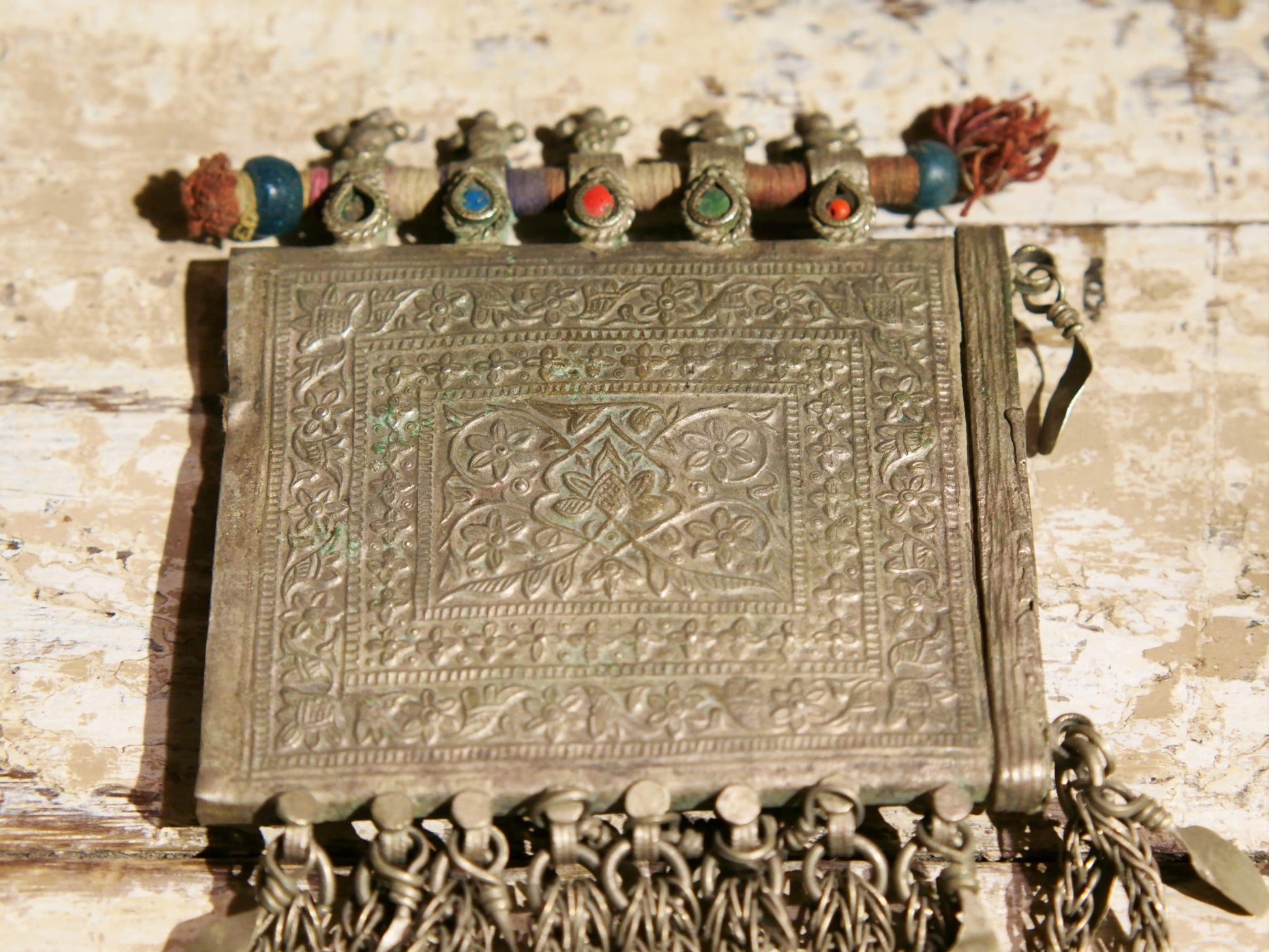 La sezione superiore ha applicate sette ganci decorativi con finale rotondo .  La scatola si apre ad un'estremità e ha un cilindro di rame argento per l'inserimento di oggetti protettivi magici e "mantra".( questo taviz è stato sigillato in modo da non perdere parte dell'oggetto )