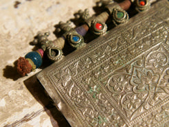 La sezione superiore ha applicate sette ganci decorativi con finale rotondo .  La scatola si apre ad un'estremità e ha un cilindro di rame argento per l'inserimento di oggetti protettivi magici e "mantra".( questo taviz è stato sigillato in modo da non perdere parte dell'oggetto )