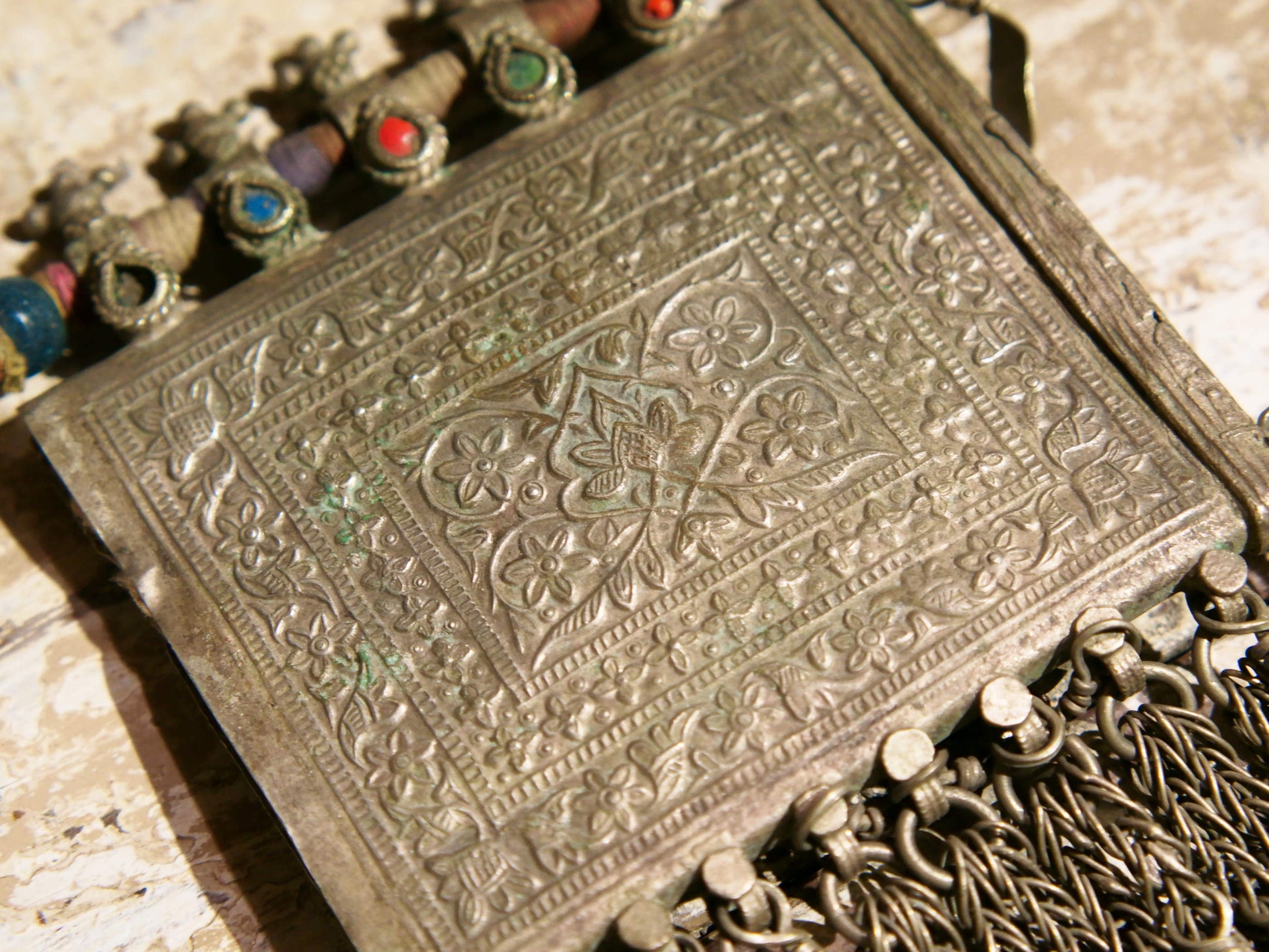 La sezione superiore ha applicate sette ganci decorativi con finale rotondo .  La scatola si apre ad un'estremità e ha un cilindro di rame argento per l'inserimento di oggetti protettivi magici e "mantra".( questo taviz è stato sigillato in modo da non perdere parte dell'oggetto )