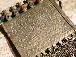 La sezione superiore ha applicate sette ganci decorativi con finale rotondo .  La scatola si apre ad un'estremità e ha un cilindro di rame argento per l'inserimento di oggetti protettivi magici e "mantra".( questo taviz è stato sigillato in modo da non perdere parte dell'oggetto )
