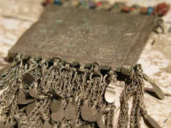 La sezione superiore ha applicate sette ganci decorativi con finale rotondo .  La scatola si apre ad un'estremità e ha un cilindro di rame argento per l'inserimento di oggetti protettivi magici e "mantra".( questo taviz è stato sigillato in modo da non perdere parte dell'oggetto )