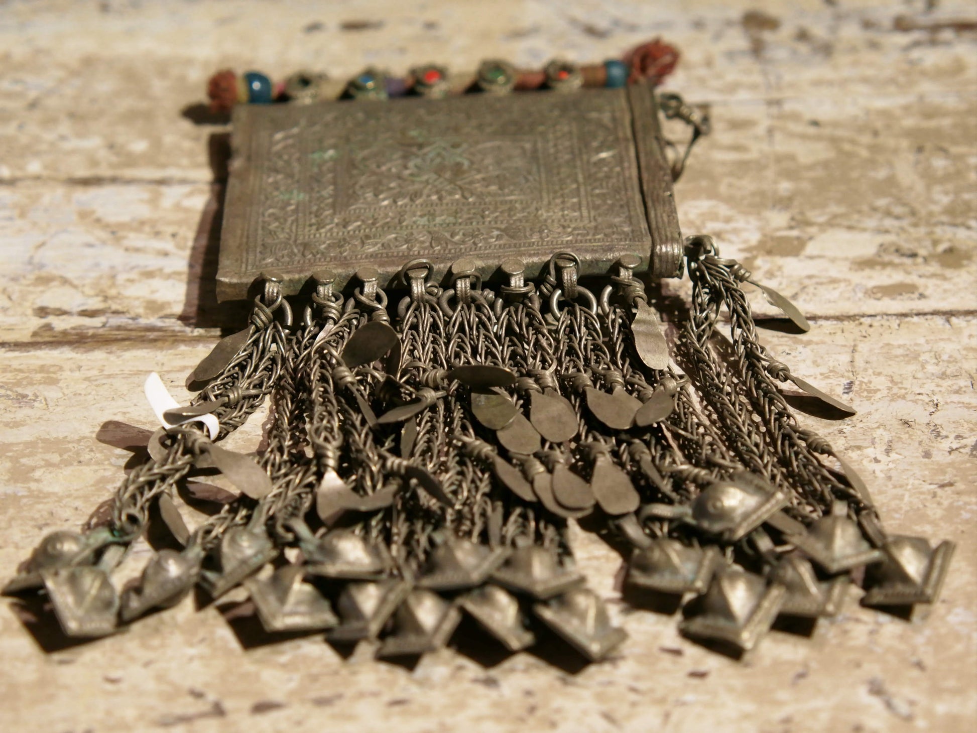 La sezione superiore ha applicate sette ganci decorativi con finale rotondo .  La scatola si apre ad un'estremità e ha un cilindro di rame argento per l'inserimento di oggetti protettivi magici e "mantra".( questo taviz è stato sigillato in modo da non perdere parte dell'oggetto )