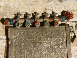 La sezione superiore ha applicate sette ganci decorativi con finale rotondo .  La scatola si apre ad un'estremità e ha un cilindro di rame argento per l'inserimento di oggetti protettivi magici e "mantra".( questo taviz è stato sigillato in modo da non perdere parte dell'oggetto )