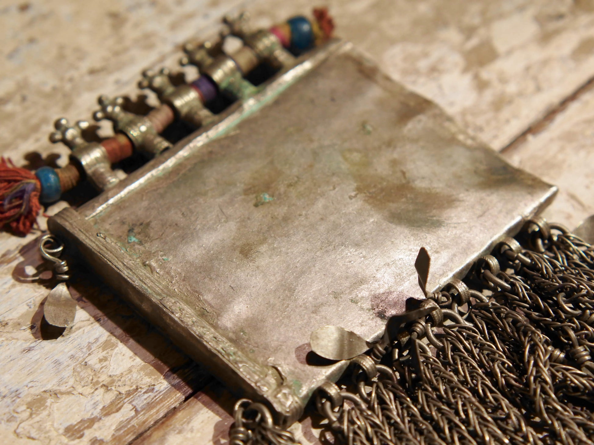 La sezione superiore ha applicate sette ganci decorativi con finale rotondo .  La scatola si apre ad un'estremità e ha un cilindro di rame argento per l'inserimento di oggetti protettivi magici e "mantra".( questo taviz è stato sigillato in modo da non perdere parte dell'oggetto )