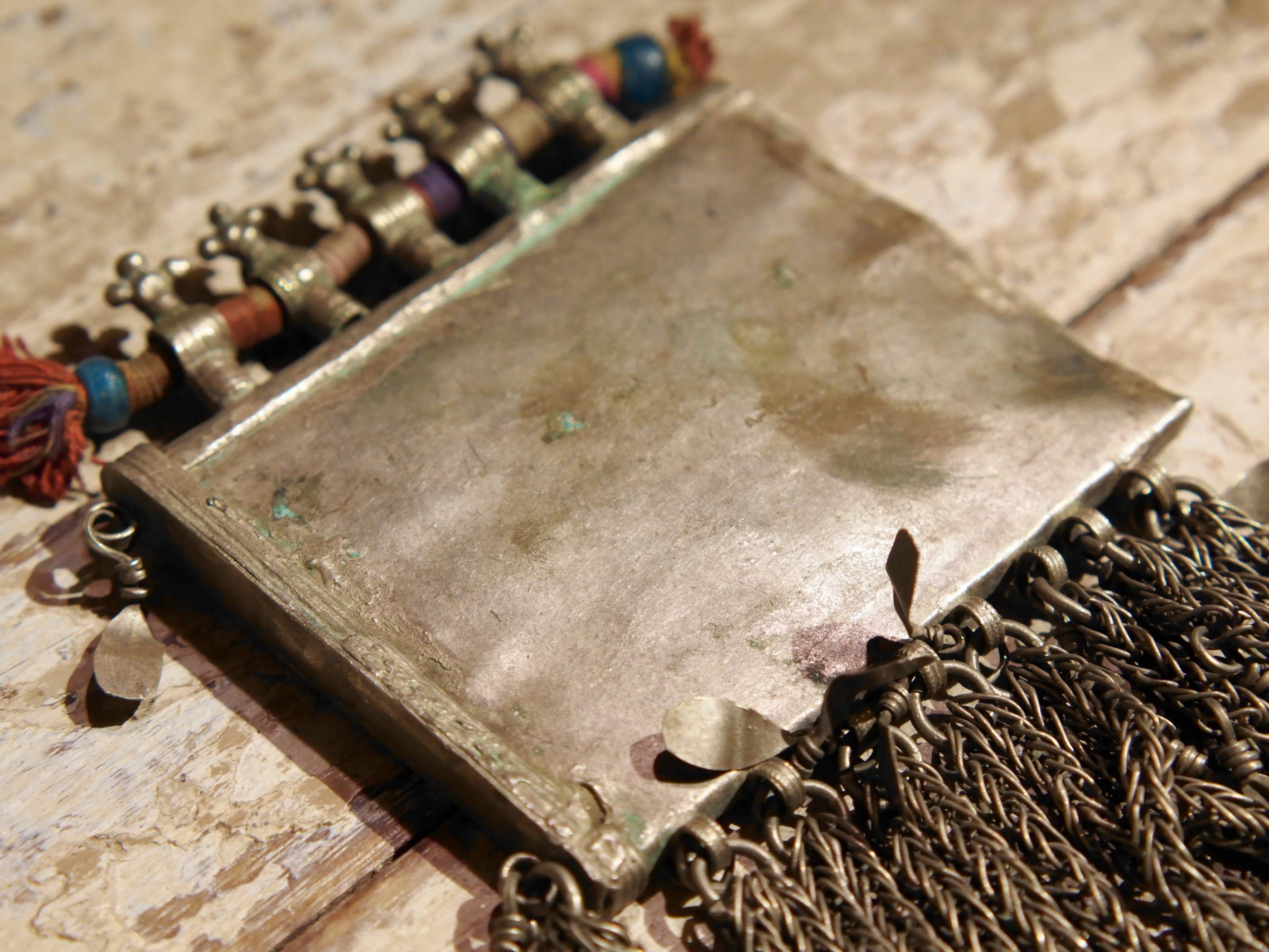 La sezione superiore ha applicate sette ganci decorativi con finale rotondo .  La scatola si apre ad un'estremità e ha un cilindro di rame argento per l'inserimento di oggetti protettivi magici e "mantra".( questo taviz è stato sigillato in modo da non perdere parte dell'oggetto )