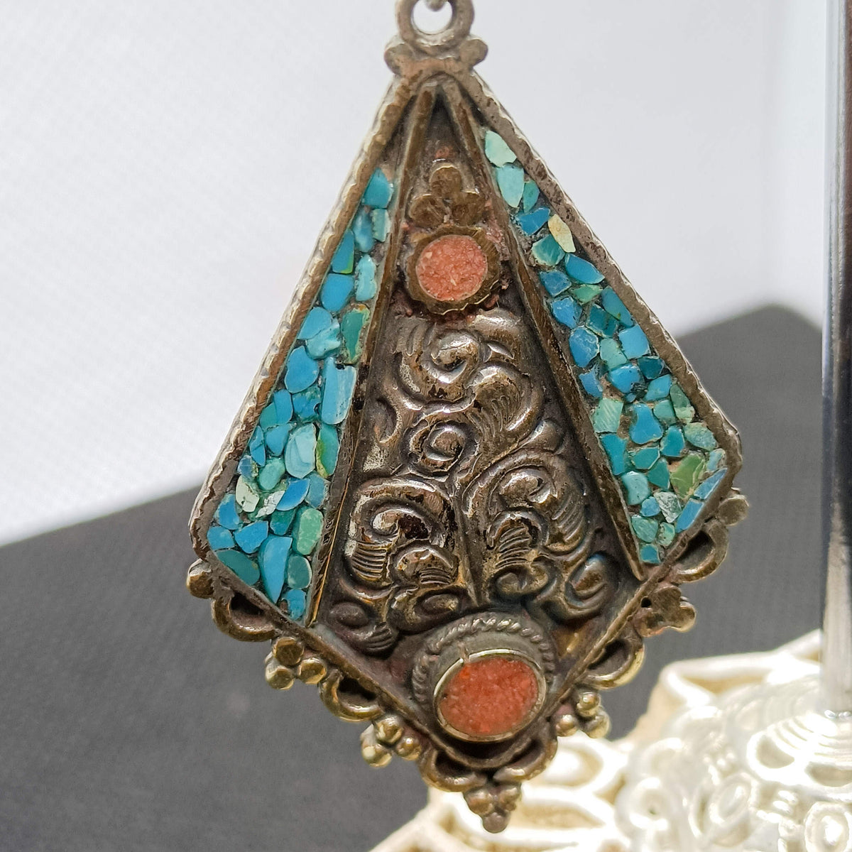 Primo piano di orecchino pendente artigianale nepalesi e tibetano in argento, german silver, corallo e turchese. cod.ONCT