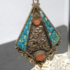 Primo piano di orecchino pendente artigianale nepalesi e tibetano in argento, german silver, corallo e turchese. cod.ONCT