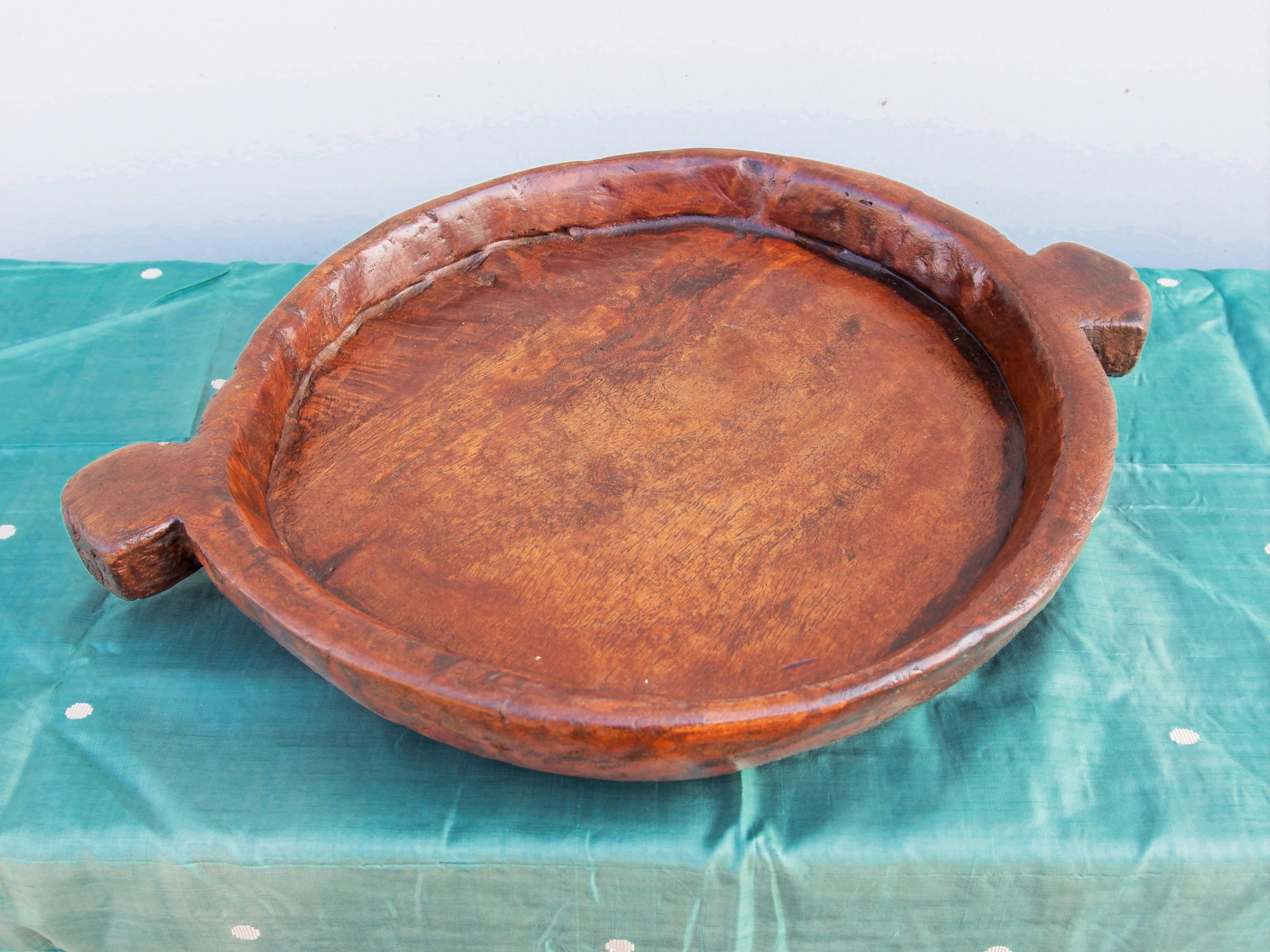 piatto in legno con manico ricavato da un unico tronco di legno.  usato in principio come piatto , setaccio per esiccare i cereali .  tronco unico di teak massello databile inizio / metà 900 .  dimensioni 40x54xh6cm.    disponibili vari modelli , contattare per info ed ulteriori foto info@etniko.it 0039 3338778241 fb/ig : etnikobycrosato